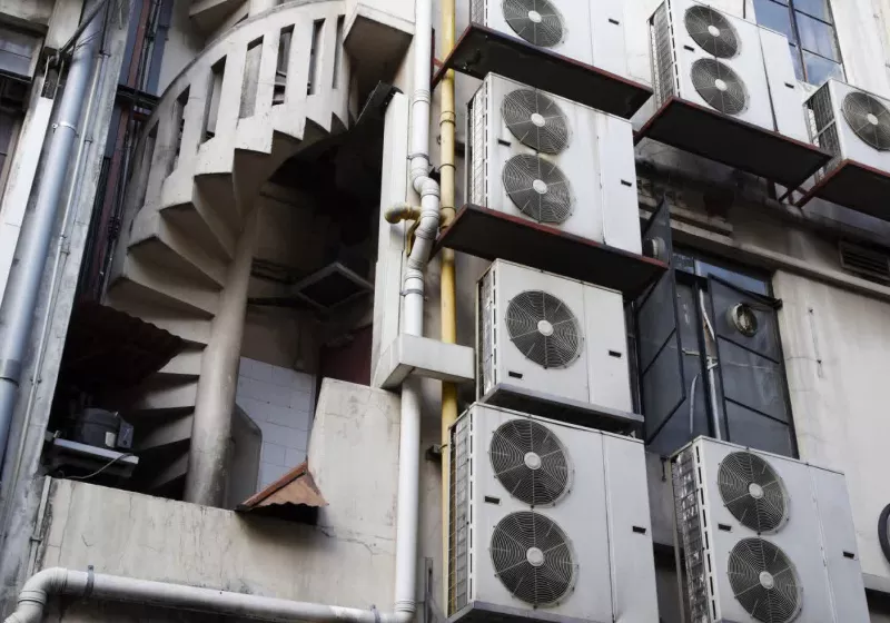 A close-up of a residential or commercial building's exterior, heavily equipped with air conditioning units and a distinct spiral fire escape or service stair.