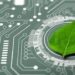 A fresh green leaf placed on an electronic circuit board with glowing lines, representing the integration of nature and technology or sustainable tech.