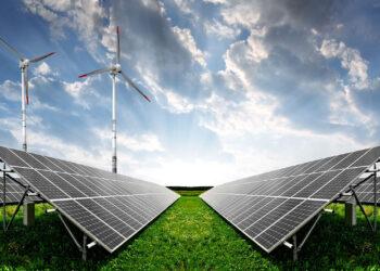 Solar panels and wind turbines in a green field under a cloudy sky, representing renewable energy.